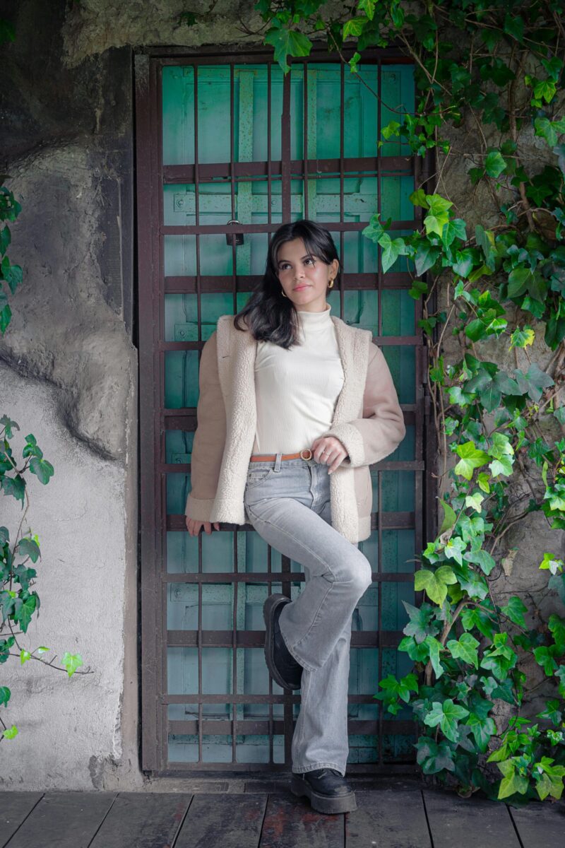 Stylish woman poses by vine-covered rustic doorway in Costa Rican setting.