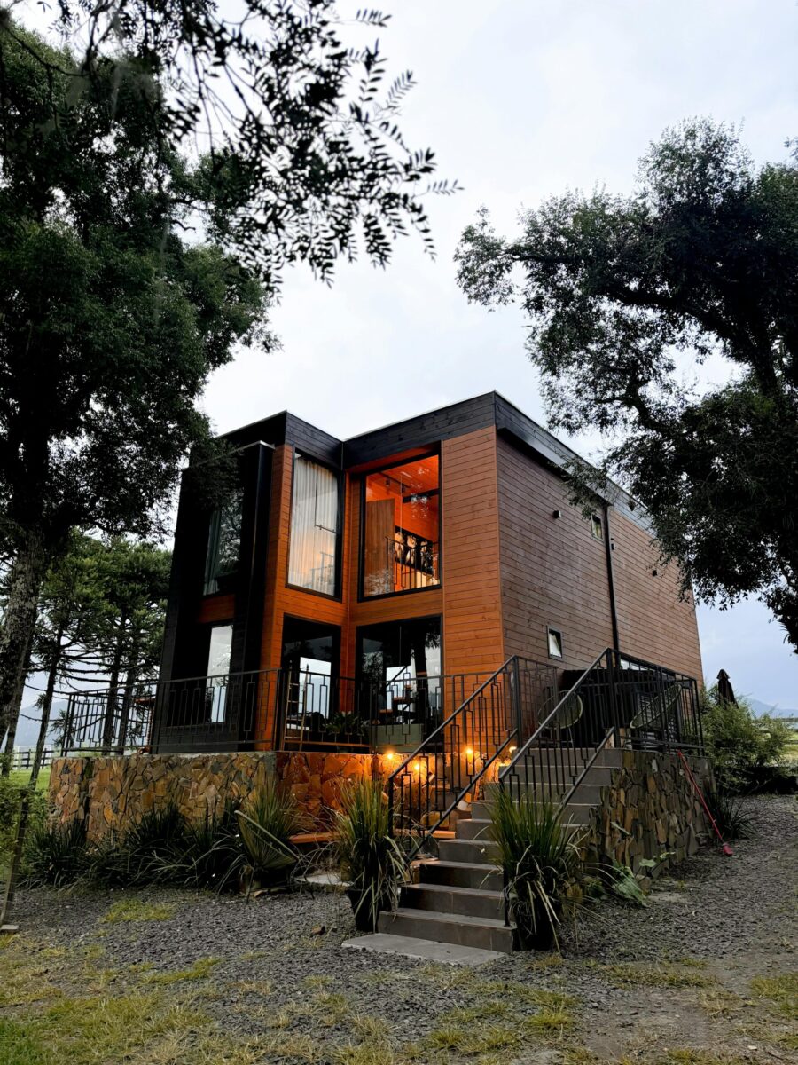 A contemporary wooden cabin with warm lighting nestled among trees, creating a cozy outdoor atmosphere.