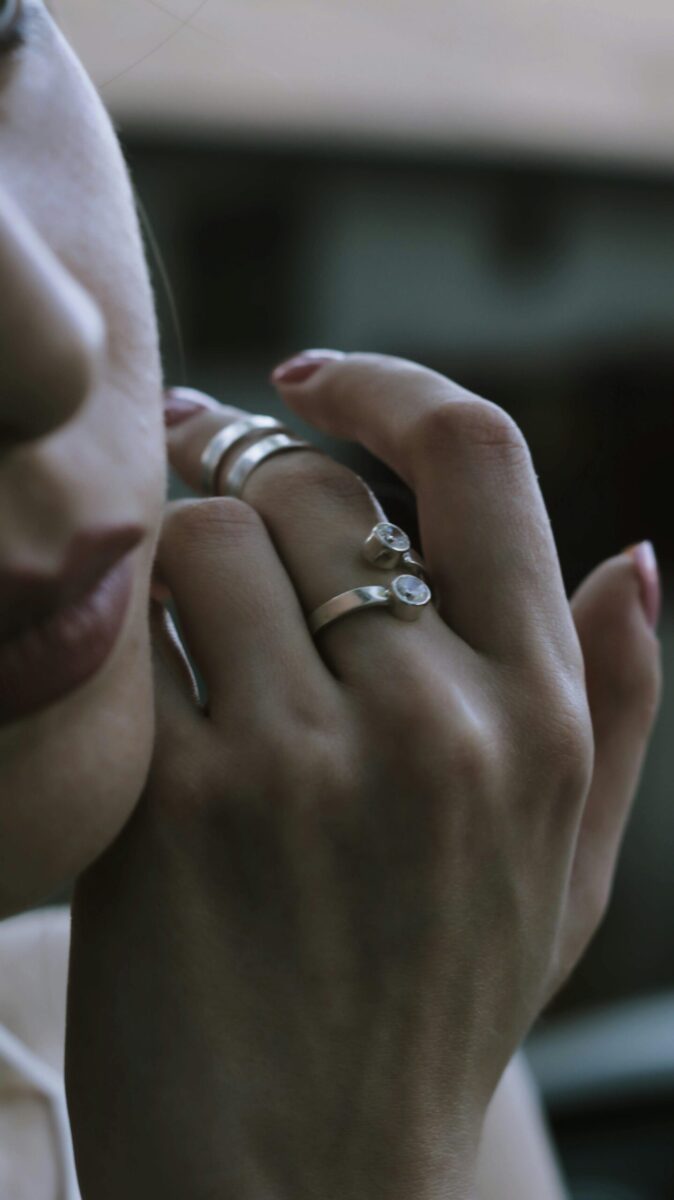 Crop anonymous female showing stylish accessories on hand while touching face on blurred background