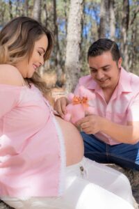 Happy pregnant couple bonding outdoors, enjoying a sunny day and holding a teddy bear.